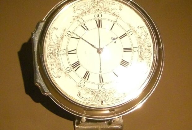 John Harrison’s H4 marine timekeeper, showing its white Roman-numeral dial and silver case, on museum display at Greenwich.