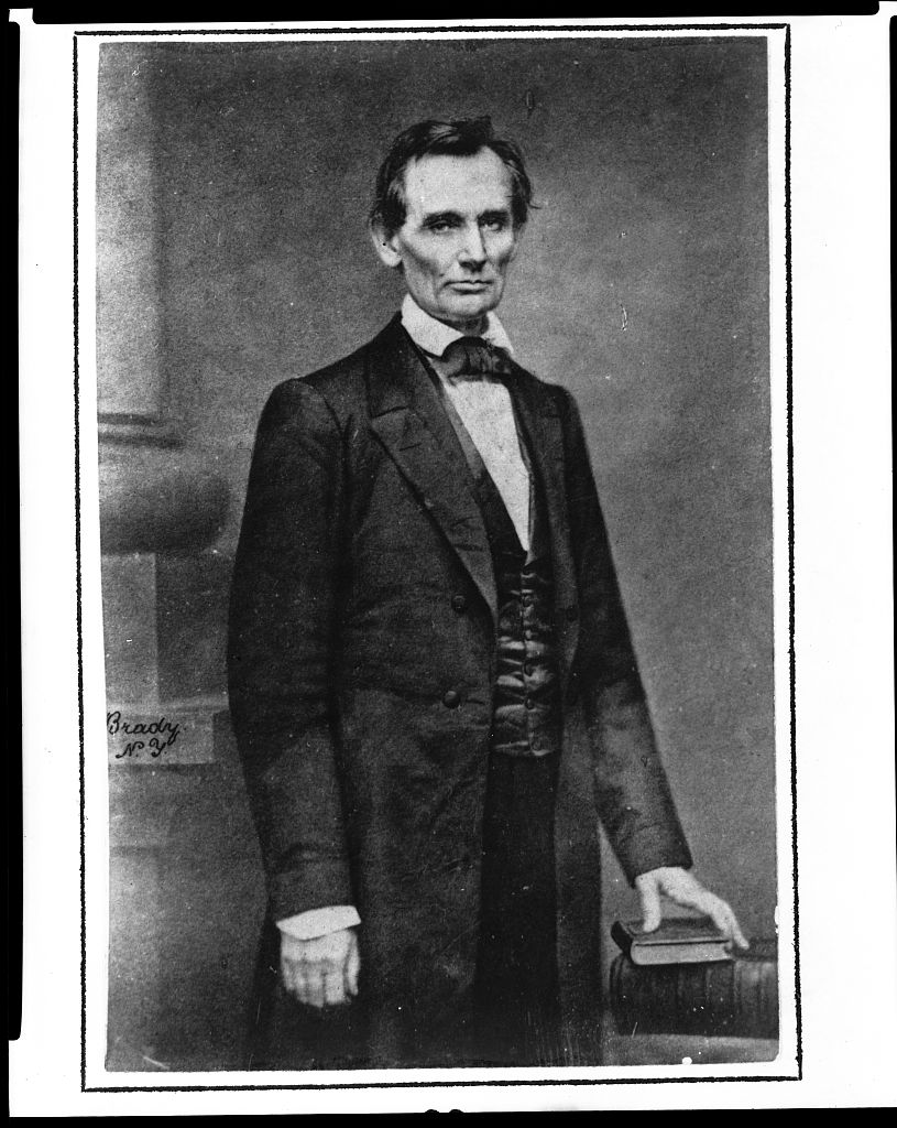 Mathew Brady's three-quarter-length portrait of a beardless Abraham Lincoln standing beside a table, photographed in 1860.