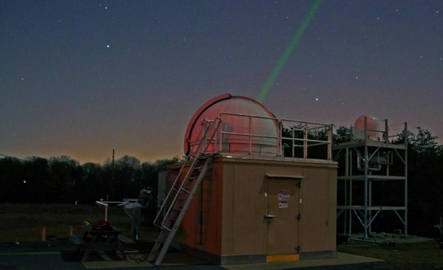 NASA Goddard laser-ranging observatory projecting a green laser into the night sky