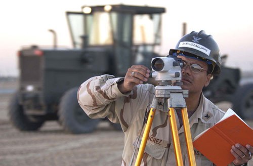 U.S. Navy engineering aide using an optical survey level on a tripod in the field