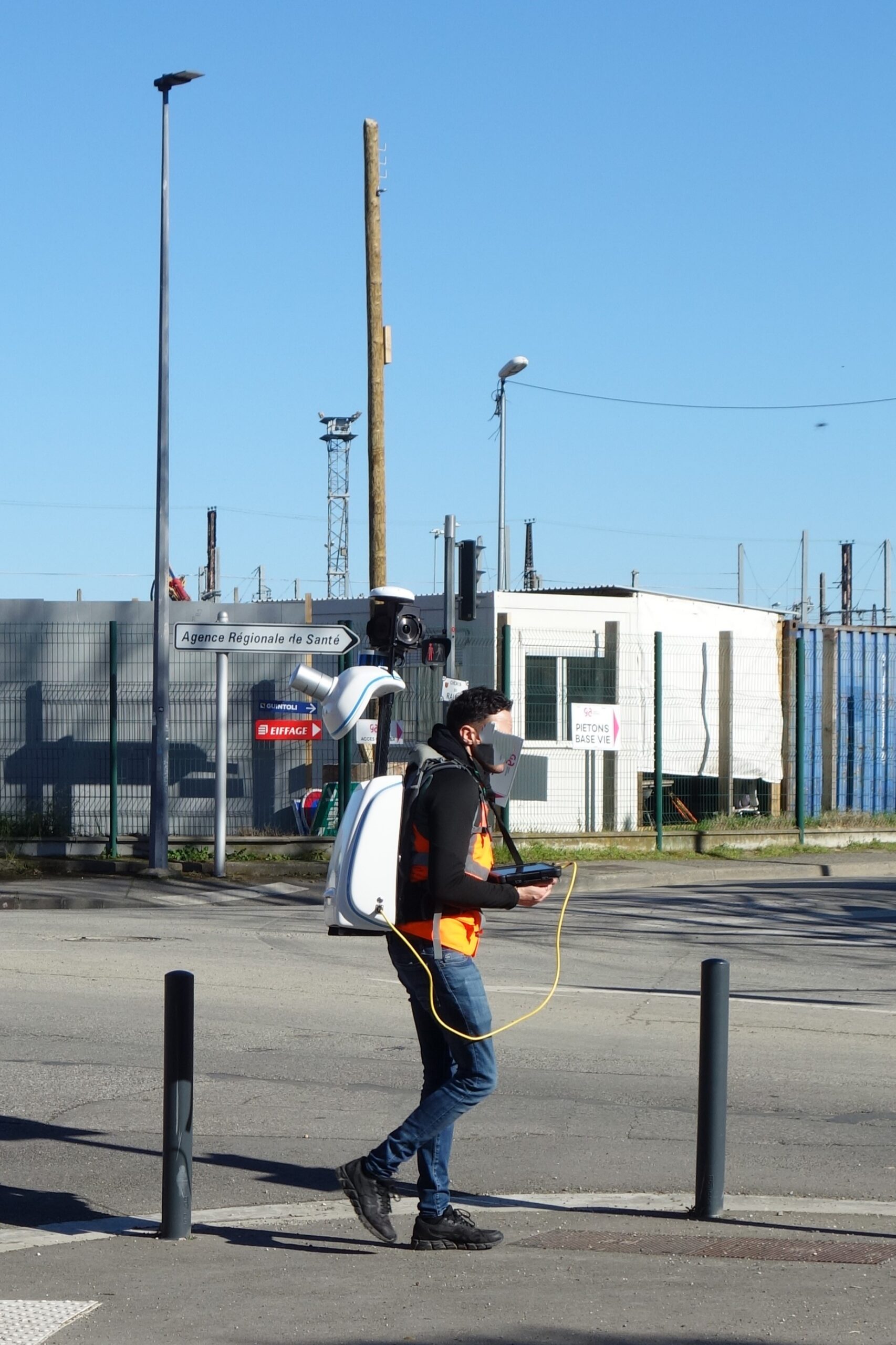 A person walks through a street wearing a backpack-mounted mapping sensor assembly.