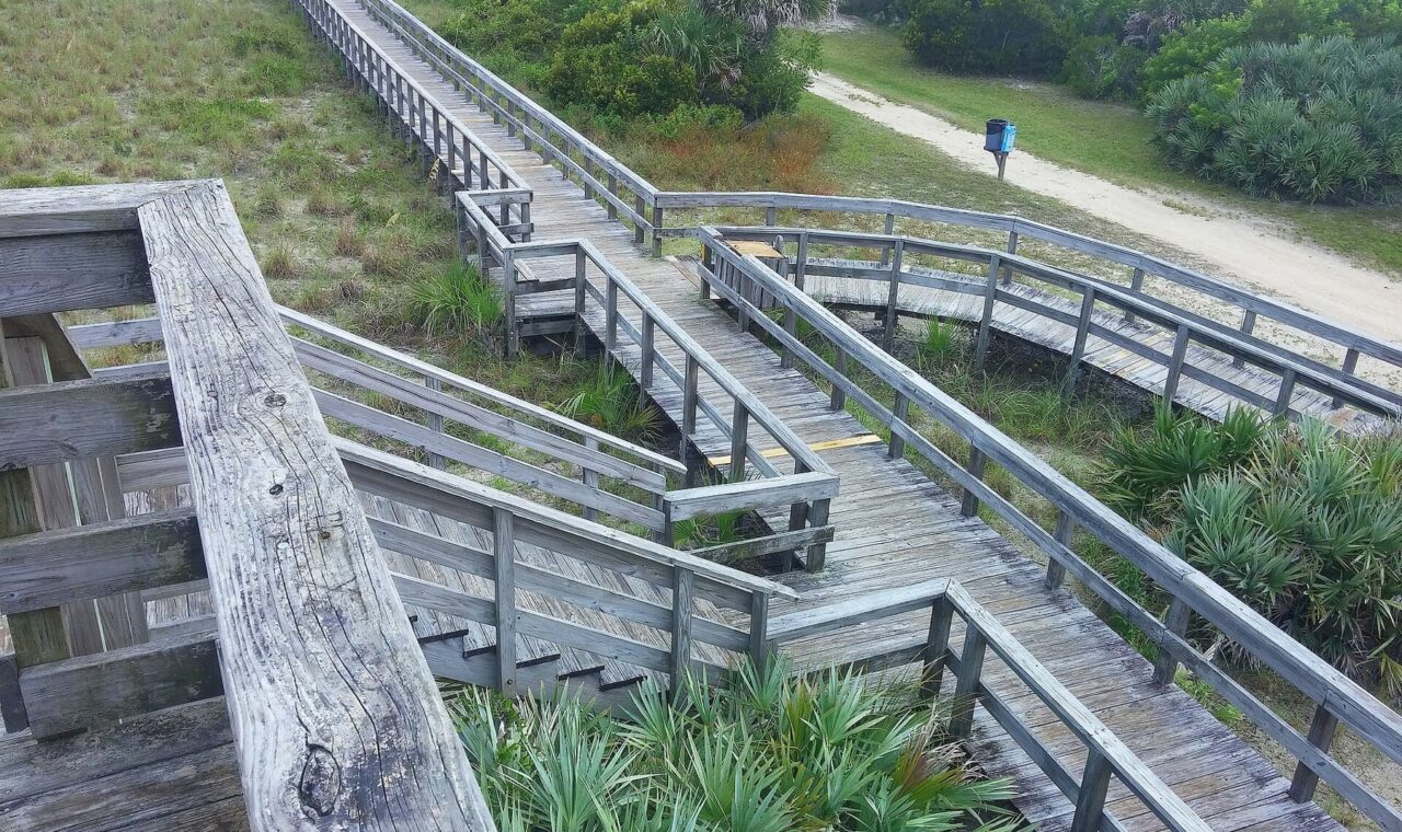 Wooden boardwalk with railings crosses vegetated dunes at Smyrna Dunes in Florida.