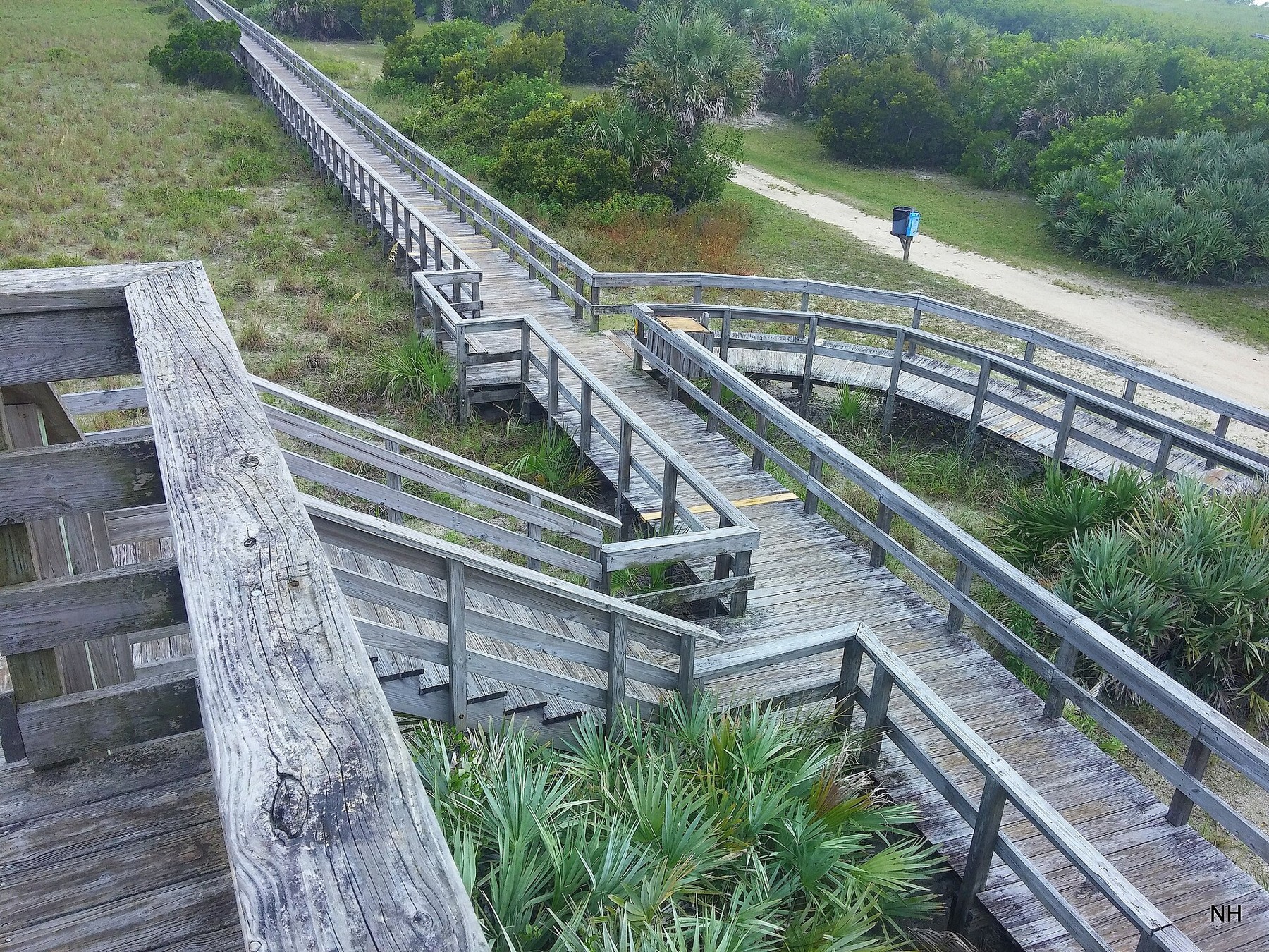 Wooden boardwalk with railings crosses vegetated dunes at Smyrna Dunes in Florida.