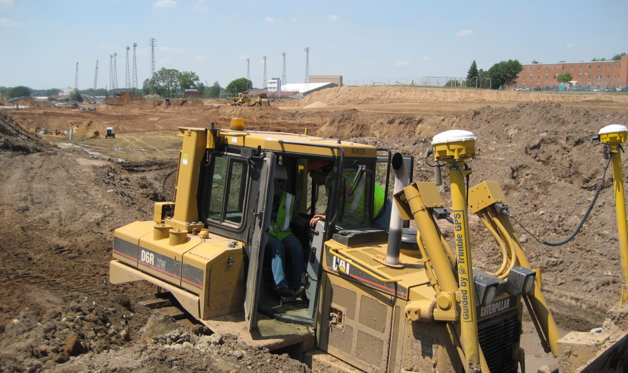 A bulldozer at a road construction site has two yellow-and-white positioning receivers mounted above its blade.