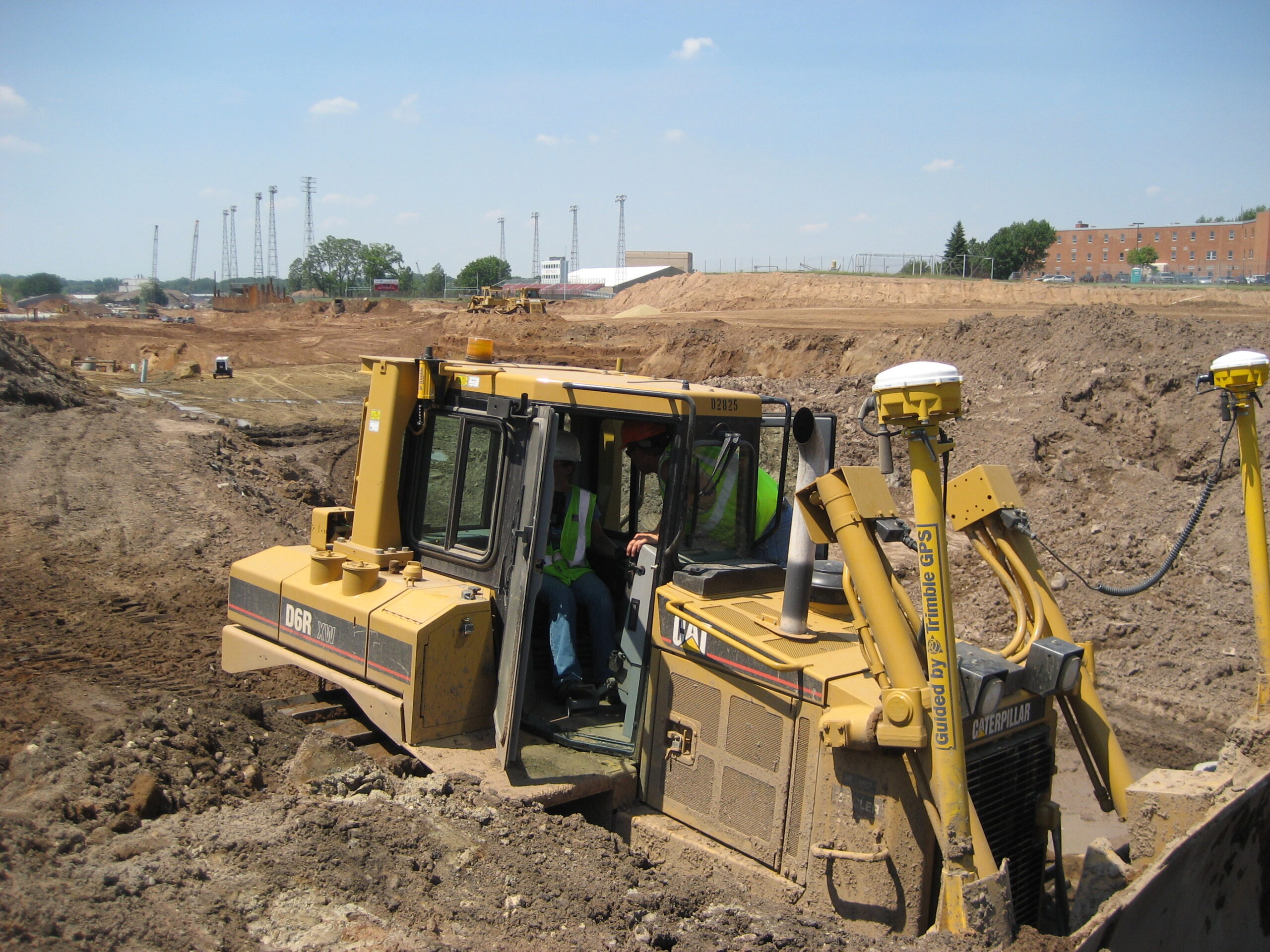 A bulldozer at a road construction site has two yellow-and-white positioning receivers mounted above its blade.