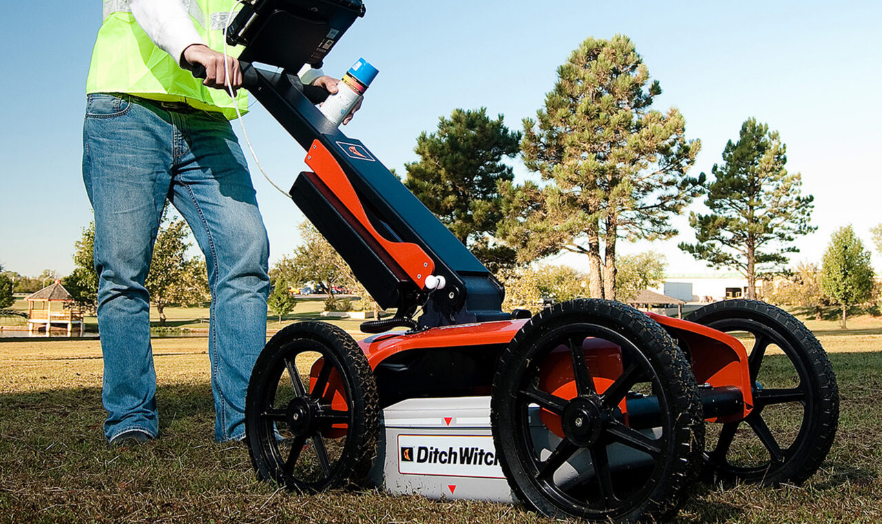 An operator pushes a wheeled ground-penetrating radar unit across an open field.