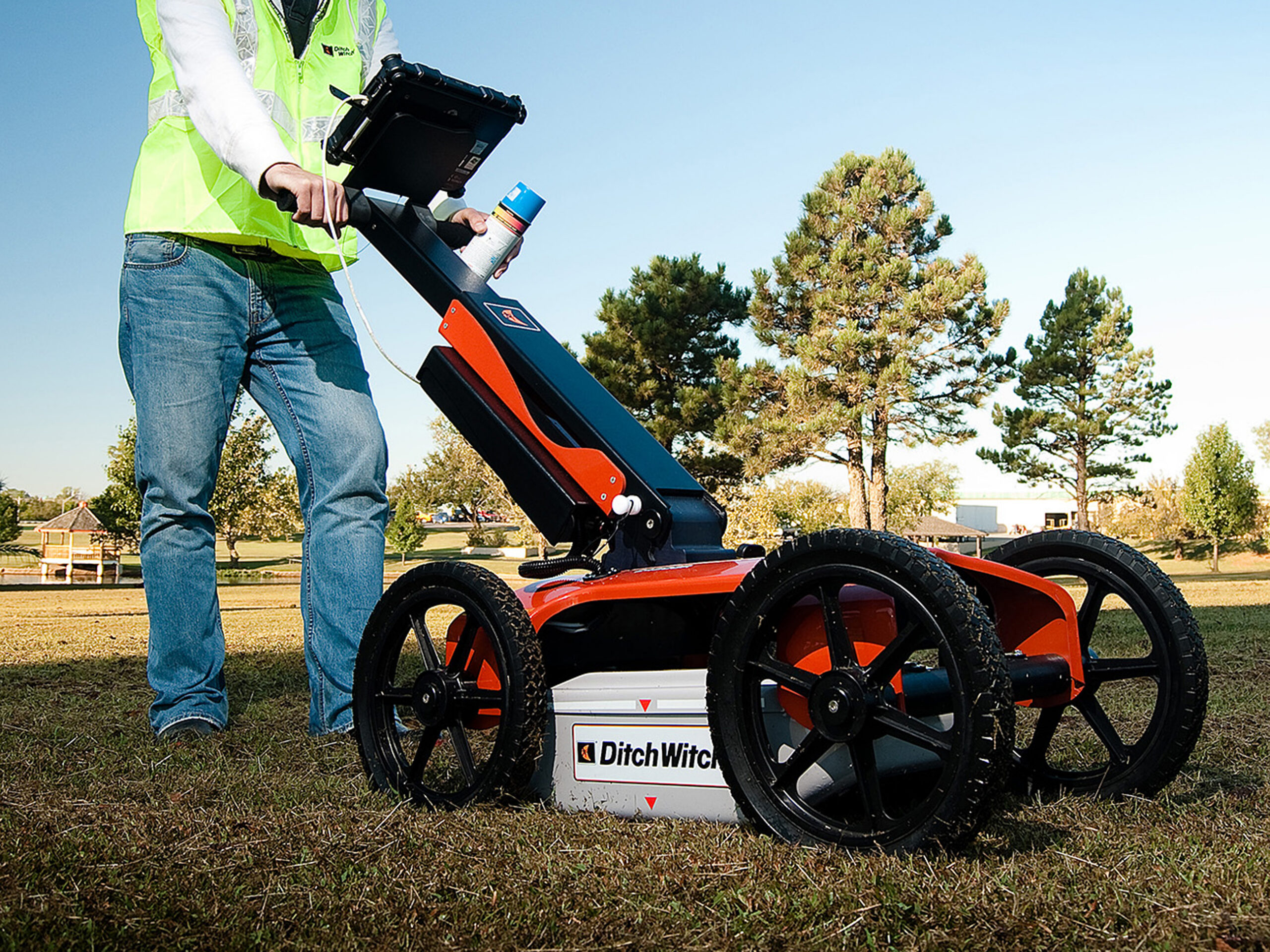 An operator in a high-visibility vest pushes a wheeled radar instrument across grass.