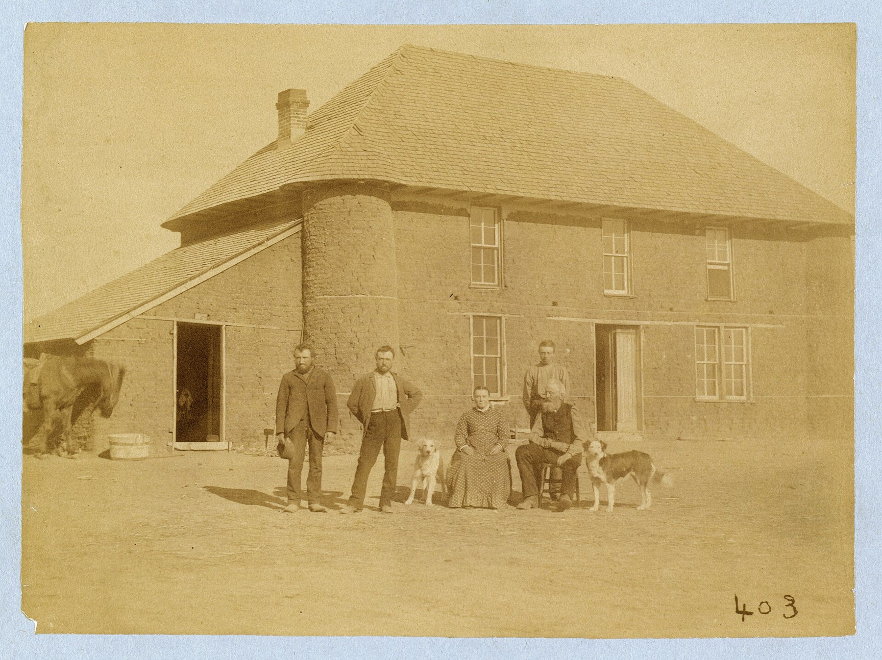 The Haumont family and dogs posed in front of a two-story sod house with a broad shingled roof in Nebraska in 1886.