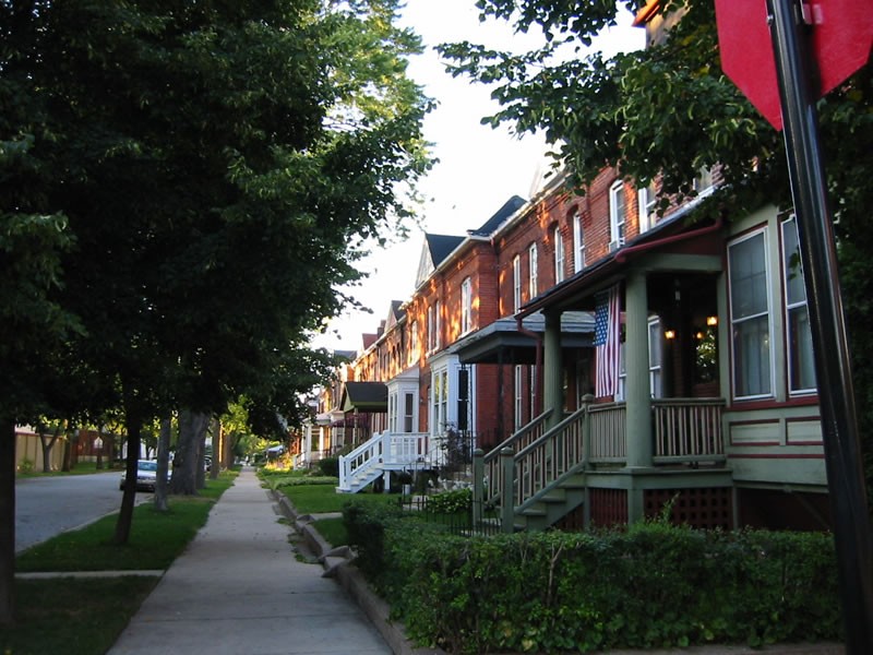 Brick Pullman rowhouses with front porches along a tree-lined Chicago sidewalk.