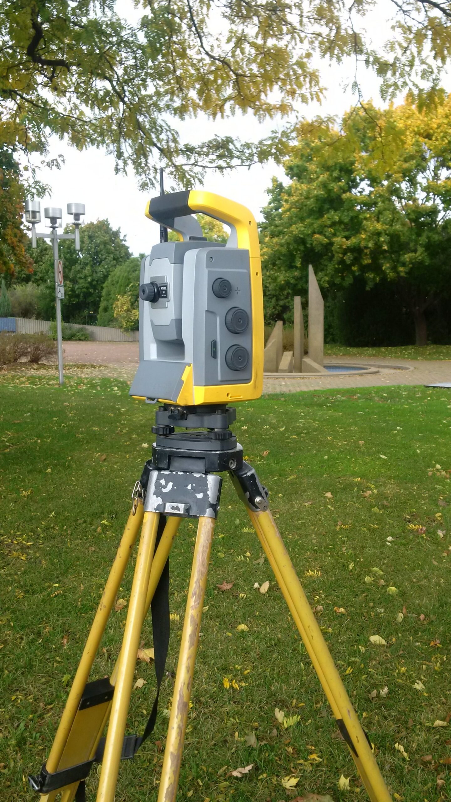 A yellow and gray robotic total station stands on a yellow tripod in a grassy setting.